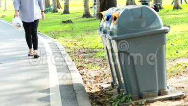 亚洲女人从地板上捡垃圾到垃圾桶，女人在公园的草地上捡垃圾塑料袋，